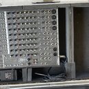Šedý mixážní pult značky SAMSON, model MixMaster 12, umístěný v černé transportní skříni. Zařízení má řadu faderů, otočných knoflíků a vstupních kone…