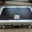 Černý transportní flightcase s hliníkovými hranami a kovovými rohy. Uprostřed horní strany je nalepený bílý štítek s nápisy TRANSPORT CASE, CUSTOM FL…