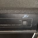 Detailní pohled na horní část basového komba s černým texturovaným povrchem. Na černém ovládacím panelu je nápis PROFESSIONAL BASS COMBO, přepínač PO…