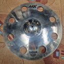 Kovový činel s otvory v okolí okraje. Na povrchu jsou viditelné nápisy AAX a O-Zone Crash 18" Medium, v dolní části je logo SABIAN. Povrch vykazuje z…