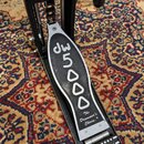 Černý bicí pedál s kovovými prvky. Na šlapadle je bílým nápisem značka dw a model 5000, dále text The Drummer's Choice.® a logo dw na horní části kon…