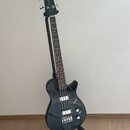 Černá elektrická basová kytara s tmavým hředníkem, umístěná na černém stojanu. Na hlavě nástroje je zlatý nápis GRETSCH a na těle bílé logo GRETSCH.…