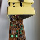 Žlutý efekt pedál s černým ovládacím knoflíkem, který je rozložený a má vyjmutou základní desku s elektronickými součástkami. Na hnědé desce je v dol…