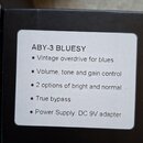 Fotografie detailu černé krabice s bílou nálepkou. Na nálepce je text: ABY-3 BLUESY, Vintage overdrive for blues, Volume, tone and gain control, 2 op…