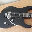 Černá elektrická kytara s dvěma humbuckery a chromovaným mostem typu Floyd Rose. Na hrazence je vidět nápis "S85". Kytara má jeden ovládací knoflík a…