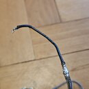 Detailní záběr na poškozený elektrický kabel s černým opletením. V horní části je kabel přetržen a viditelné jsou vytržené kovové vodiče. Kabel leží…