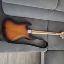 Zadní strana elektrické basy s lakovaným povrchem v přechodové barvě od žluté přes oranžovou k černé. Na hlavě nástroje je viditelné logo Fender. K b…