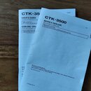 Fotografie zobrazuje dva tištěné návody k obsluze v modré barvě. Na horním listu je nápis CTK-35 a USER'S GUIDE, GUÍA DEL USUARIO. Na spodním listu j…