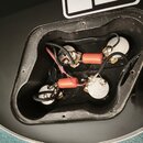 Fotografie zachycuje otevřenou elektronickou dutinu v černé elektrokitare. Uvnitř jsou vidět tři potenciometry a dva oranžové kondenzátory s nečiteln…