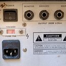 Zadávací panel šedého elektronického zařízení s nápisy POWER, MONITOR, BRIDGED a MAIN OUT. Jsou zde čtyři výstupní konektory, přepínač ON/OFF a napáj…