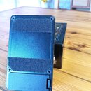 Zadní strana černého kytarového efektu s texturovaným povrchem. Ve spodní části je víčko baterie s nápisem CE BATTERY 00SP 9V. Za efektem je vidět čá…