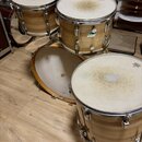 Sada bubnů s dřevěnými korpusy v přirozené barvě a kovovými obručemi. Na jednom z tomů je viditelné logo „Ludwig“. Membrány vykazují známky opotřeben…