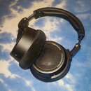 Černé studiová sluchátka s velkými polstrováním z tmavé látky. Na vnějším okraji pravého sluchátka je bílý nápis NEUMANN.BERLIN a STUDIO HEADPHONE ND…