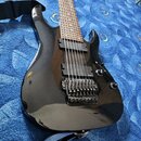Černá elektrická kytara s tmavým hnedým hmatníkem a dvěma humbuckery. Na těle je u kobylky viditelný nápis Ibanez RG. Nástroj má Floyd Rose typový ko…