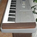 Digitální piano stříbrné barvy s dřevěnou lištou v přední části a dřevěným stojanem. Nástroj má standardní klávesnici a ovládací panel s tlačítky, po…