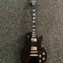 Tmavě vínová elektrická kytara s tvarem Les Paul. Na hlavě je viditelné logo Gibson, hradlo a ladicí kolíky jsou v zlatém provedení. Kytara má dva hu…