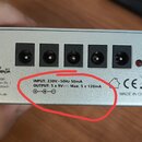 Detail stříbrného kovového zařízení s pěti černými kulatými konektory. Na spodní části je nápis: „INPUT: 230V~50Hz 50mA OUTPUT: 5 x 9V⎓ Max. 5 x 120m…