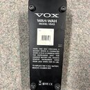 Zadní strana černého efekt pedálu Wah-Wah. Na povrchu je bílý nápis VOX WAH-WAH MODEL V845 a v dolní části text s instrukcemi k výměně baterie, značk…