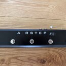 Černý MIDI kontrolér s pěti kovovými spínači. Na horní straně je bílý nápis AIRSTEP a vedle něj v rámečku označení TX. Zařízení je umístěno na dřevěn…