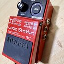 Červený efekt pedál s černým spínacím pedalem a ovládací sekcí. Na zařízení jsou nápisy „Loop Station“, „RC-1“ a logo „BOSS“. Horní panel obsahuje ov…