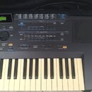 Černý elektronický klávesový nástroj s bílými a černými klávesami. Horní panel obsahuje zahlreiche tlačítka, posuvníky a displej s nápisy jako MUSIC…