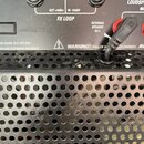 Detail zadní strany černého kytarového komba s kovovou perforovanou mřížkou. V horní části jsou konektory a ovládací prvek s nápisy RETURN, LEVEL, SE…