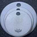Tři bílé bubnové skins různých průměrů položené na šedém povrchu. Na horním a prostředním skinu je černé logo MAPEX, na spodním skinu je nápis MAPEX…