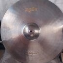 Kruhová kovová činely v stříbrné barvě s viditelným broušením povrchu. V horní části je zlatý nápis Zildjian ZBT a v dolní části logo Zildjian. Nástr…