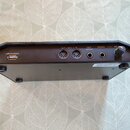 Zadní strana černého elektronického hudebního zařízení. Jsou zde viditelné konektory s nápisy USB STORAGE, OUT, MIDI, IN, FOOT SWITCH a PHONES, dále…