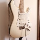 Bílá elektrická kytara typu Stratocaster s bílým pickguardem a světle hnědým hmatníkem. Nástroj má tři snímače, tři bílé ovládací knoflíky a chromova…