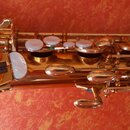 Detailní pohled na mechanismus zlatého saxofonu. Jsou vidět klapy s perleťovými vložkami a kovové spojovací části. Na nástroji nejsou žádné čitelné z…