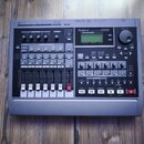 Šedý digitální záznamový studiový systém s nápisem Roland VS-840 DIGITAL STUDIO WORKSTATION. Zařízení obsahuje displej, několik posuvníků, tlačítek a…