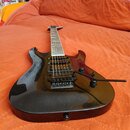 Černá elektrická kytara s lesklým povrchem a prohnutým korpusem. Nástroj má dva humbuckery, jeden potenciometr pro hlasitost a jeden pro tón, dále je…