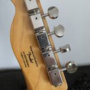 Zadní strana hlavy kytary z přírodního světlého dřeva s pěti chromovanými ladičkami. Na dřevě je černý nápis „Designed and Backed by Fender®“, pod ní…