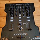 Černý DJ mixér s nápisem ALLEN&HEATH v horní části a označením XONE:23C ve spodní části. Přístroj obsahuje dva kanály s knoflíky, posuvníky a tlačítk…
