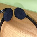 Černé on-ear sluchátka s pěnovými náušníky. Jsou vyrobeny z černého plastu a mají přiložený kabel. Na sluchátkách nejsou vidět žádné značky ani nápis…