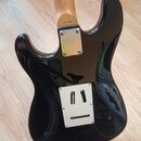 Zadní strana elektrické kytary s černým lesklým povrchem a světle hnědým krkem. Na spojení krku s tělem je kovová krytka a nad ní malý nápis "MADE IN…