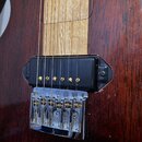 Detail korpusu elektrické kytary z tmavého dřeva s viditnou masivní strukturou. Na fotce je černý humbucker snímač a chromovaný kobylník s pružinami.…