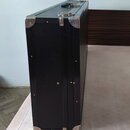 Černý tvrdý kufýr s texturovaným povrchem a kovovými hranami. V horní části jsou vidět kovové zapínání a úchyt. Na povrchu nejsou žádné viditelné zna…