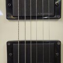 Detail elektrické kytary v krémové barvě se dvěma černými humbuckery. Na spodním snímači je v pravém dolním rohu nápis R.M.pickups, stejný nápis je v…