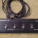 Černý nožní spínací pedalboard s šesti kovovými spínači a červenými kontrolkami. Na horní hraně je bílý nápis AdvancedValvestateTechnology a vpravo o…