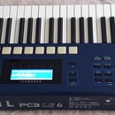 Modrý digitální klavír s bílými a černými klávesami. Na spodní hraně je bílý nápis KURZWEIL PC3 LE 6 a v pravém dolním rohu je stejný model označen j…