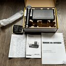 Fotografie zobrazuje černý bezdrátový mikrofon a přijímač v originální krabici s polystyrenovou výplní. Na těle mikrofonu je svisle napsáno SAMSON a…