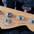 Hlava basové kytary z přírodního dřeva s čtyřmi chromovanými ladičkami. Na dřevě je černý nápis Fender® a pod ním menší text MADE IN U.S.A., vedle kt…