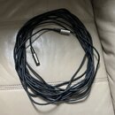 Černý kabel s kovovými konektory na obou koncích. Kabel je svinutý do kruhu a položený na světlém koženém povrchu. Na konektorech nejsou viditelné žá…