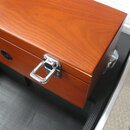 Detail hnědého dřevěného pouzdra s lesklým povrchem. Na boku je umístěn kovový stříbrný zapínací háček a tmavý oválný štítek s nečitelným nápisem. Po…