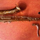 Zlatý saxofon s ornamentálním rytím na zvonu. K nástroji jsou přiloženy dvě hrdla a jedna černá krytka. Povrch je lesklý, bez viditelných značek či n…