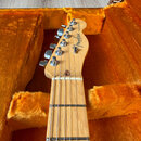 Světle hnědá elektrická kytara v oranžovém plišovém kufru. Na hlavě je černé logo Fender a nápisy TELECASTER oraz MADE IN USA. Pod logem je viditelné…