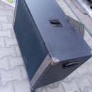 Černý obdélníkový reproduktorový box s povrchem z lakovaného dřeva. Horní strana obsahuje vestavěnou úchytovou rukojeť a na boku je umístena černá pl…