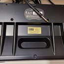 Fotografie zachycuje spodní stranu černého elektronického zařízení z plastu. Na horní části je vidět štítek s označením CE, nápisem CAN ICES-003(B)/N…